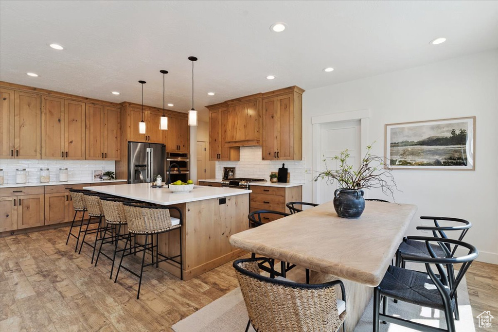 Kitchen with a kitchen bar, a kitchen island with sink, recessed lighting, light wood-style floors, and appliances with stainless steel finishes