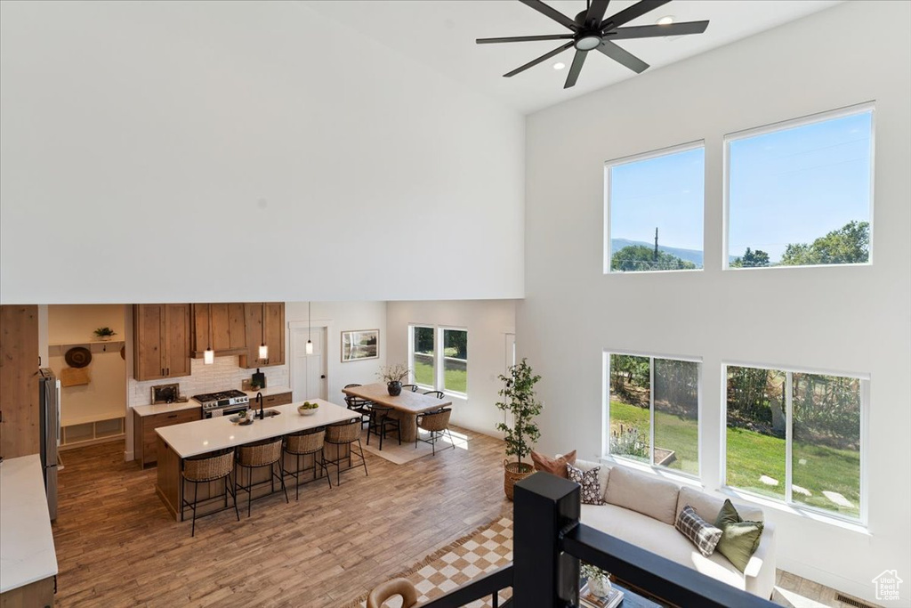 Living area with a high ceiling, a ceiling fan, light wood-style floors, healthy amount of natural light, and recessed lighting
