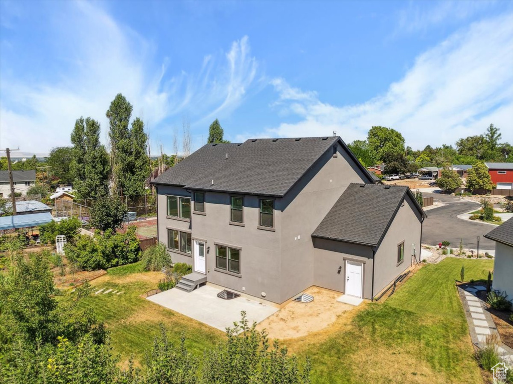 Rear view of property with roof with shingles, a patio, stucco siding, and a lawn