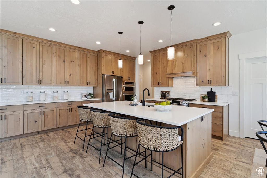 Kitchen with a kitchen bar, stainless steel appliances, backsplash, a center island with sink, and recessed lighting