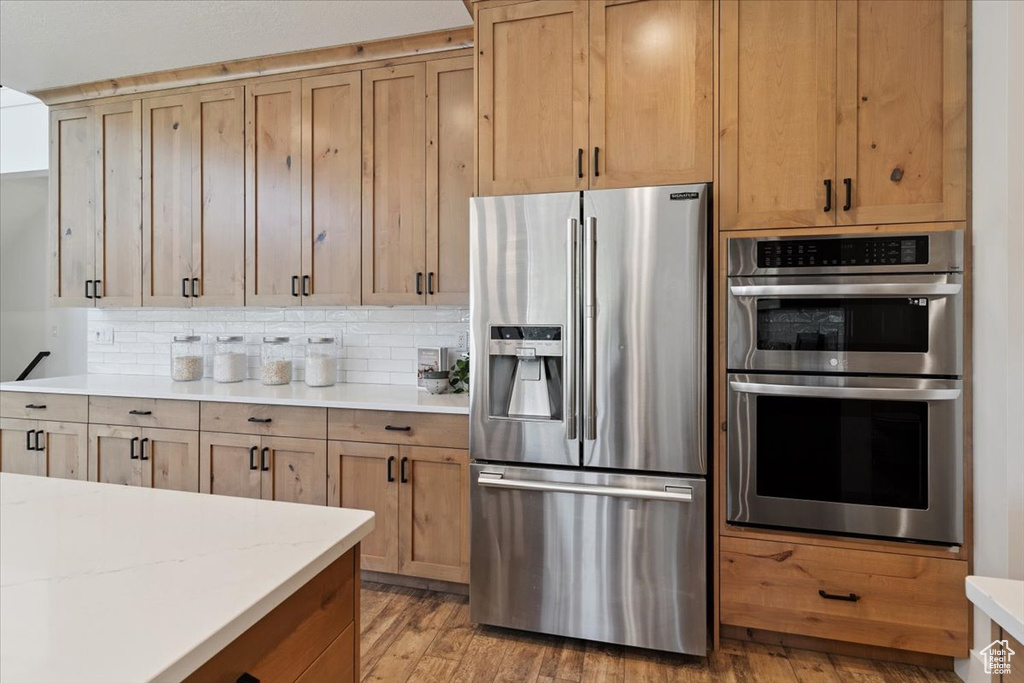 Kitchen with stainless steel appliances, light countertops, light wood-style floors, and backsplash