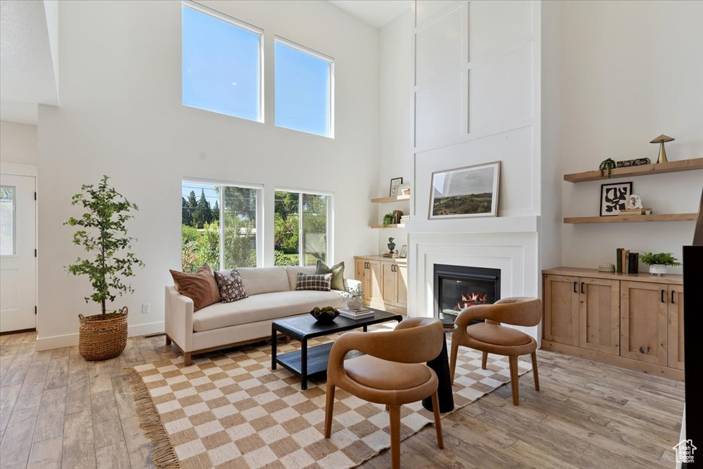 Living room with a high ceiling, light wood-style floors, and a glass covered fireplace
