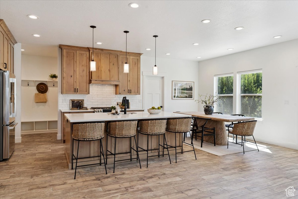 Kitchen featuring light wood-style flooring, recessed lighting, stainless steel fridge, decorative backsplash, and a breakfast bar