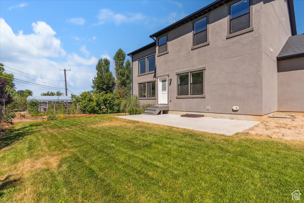 Rear view of property with stucco siding, a patio area, and a yard