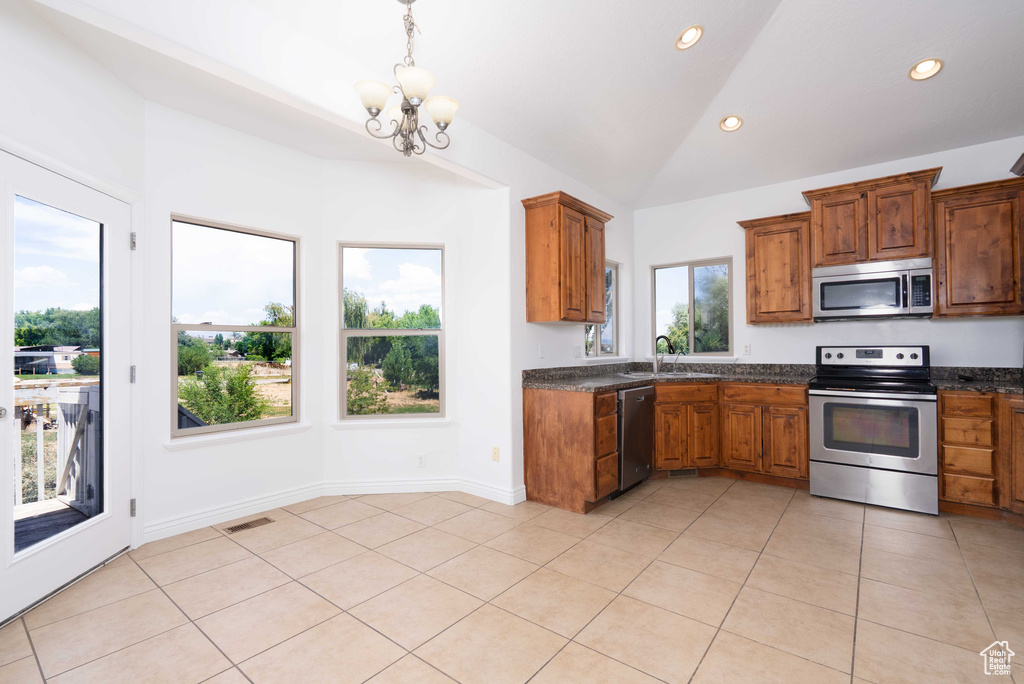 Kitchen with stainless steel appliances, dark countertops, vaulted ceiling, brown cabinetry, and a chandelier