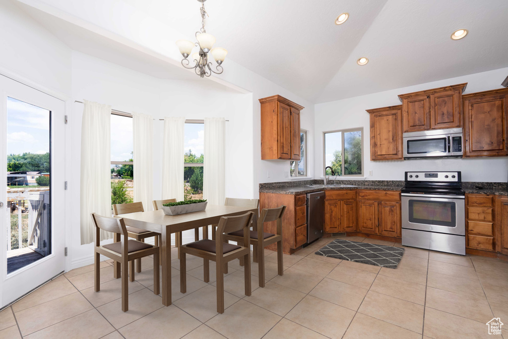 Kitchen with appliances with stainless steel finishes, dark countertops, brown cabinets, lofted ceiling, and a chandelier