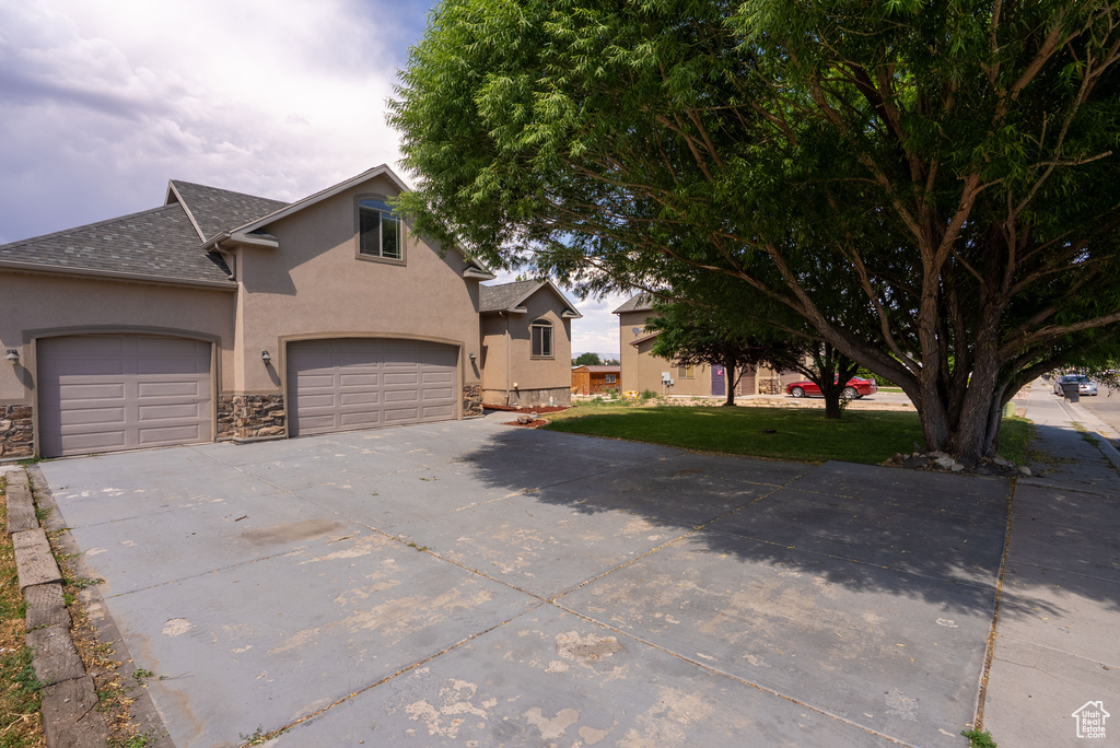 View of front of property with stucco siding, driveway, a shingled roof, and stone siding