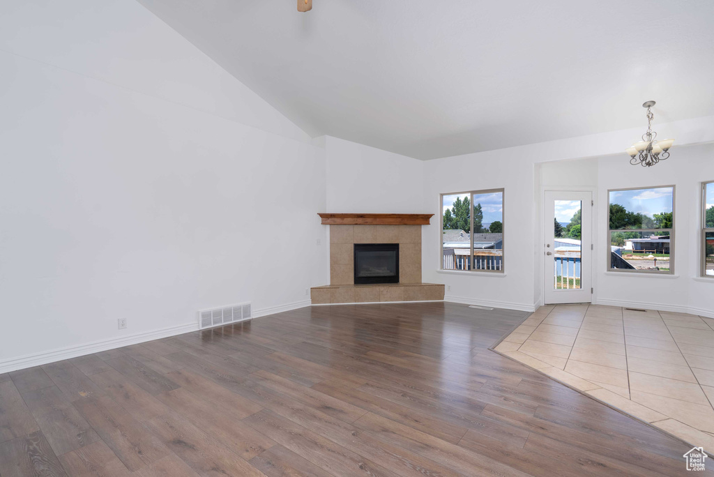 Unfurnished living room with a chandelier, wood finished floors, a tile fireplace, and lofted ceiling