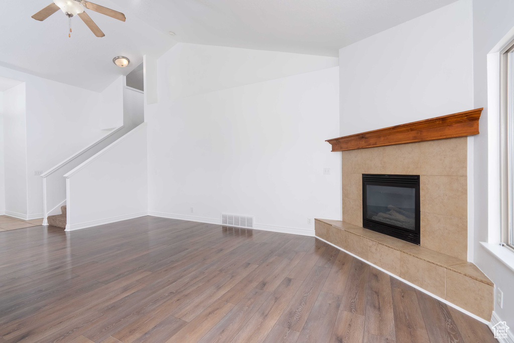 Unfurnished living room with wood finished floors, a ceiling fan, lofted ceiling, a fireplace, and stairs