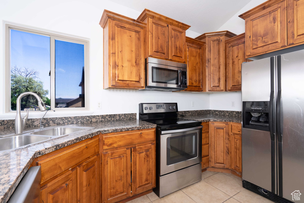 Kitchen featuring stainless steel appliances, brown cabinetry, light tile patterned flooring, and dark countertops