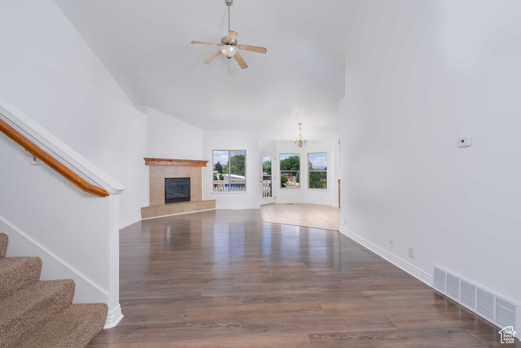 Unfurnished living room with ceiling fan, stairway, wood finished floors, a tile fireplace, and high vaulted ceiling
