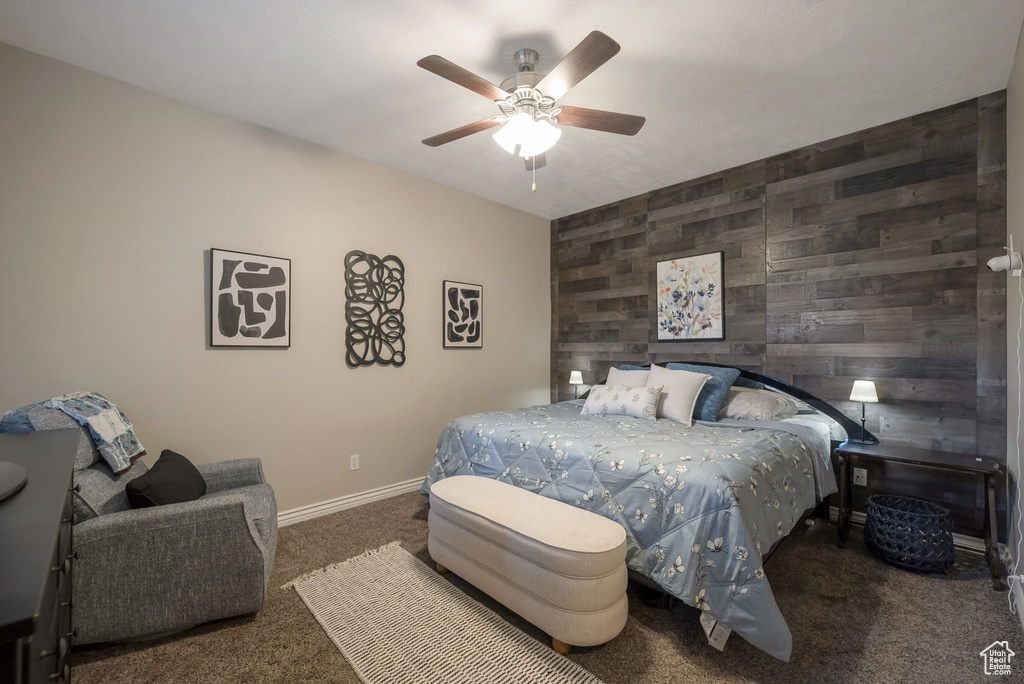 Bedroom with carpet flooring, wooden walls, ceiling fan, and an accent wall