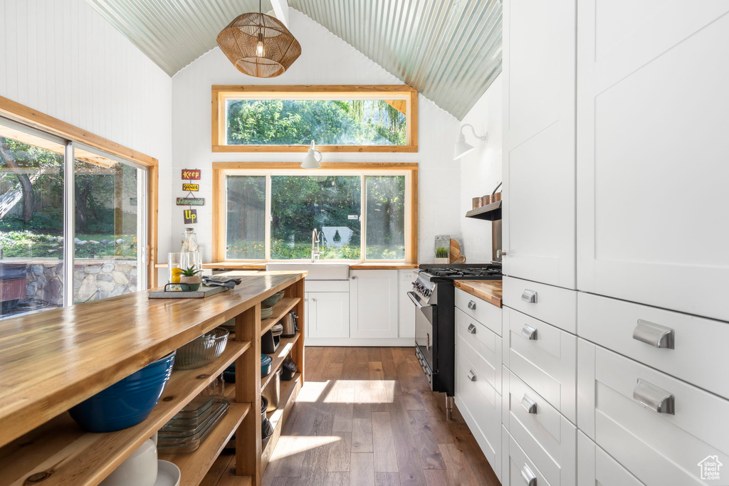 Kitchen with wooden counters, high end stove, open shelves, high vaulted ceiling, and white cabinetry