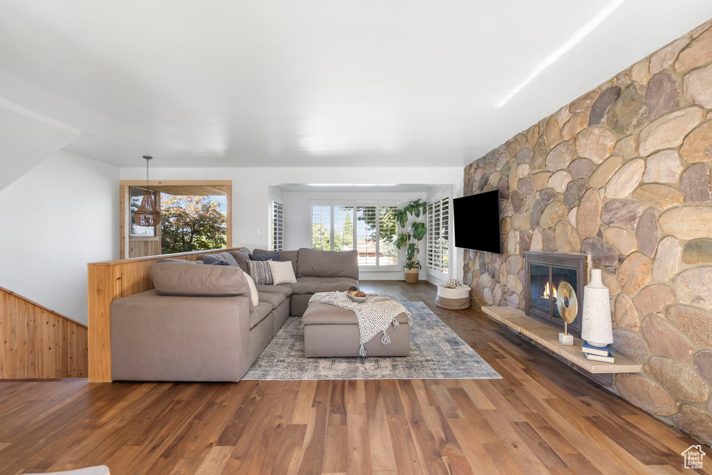 Living room featuring a stone fireplace, wood finished floors, wooden walls, and a wainscoted wall