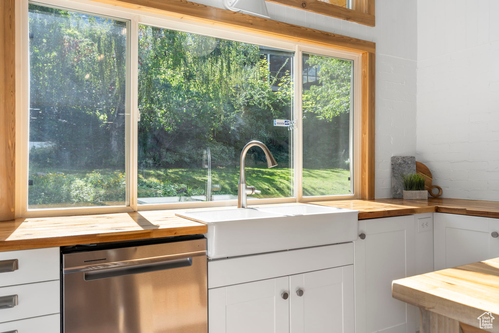 Kitchen featuring butcher block countertops, stainless steel dishwasher, and white cabinets