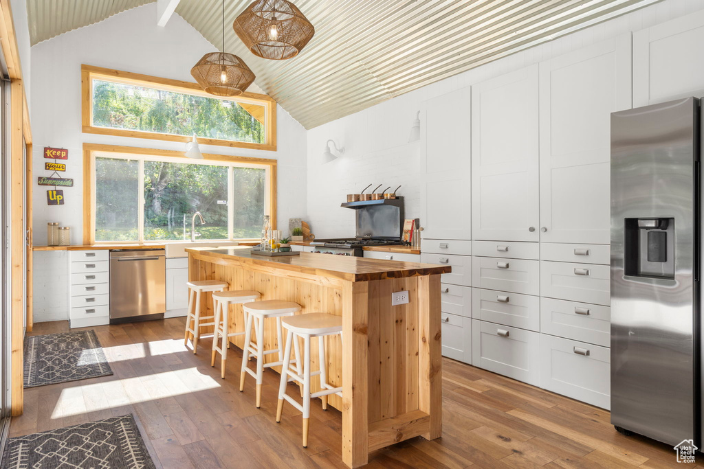 Kitchen with appliances with stainless steel finishes, butcher block countertops, high vaulted ceiling, a kitchen breakfast bar, and hardwood / wood-style flooring