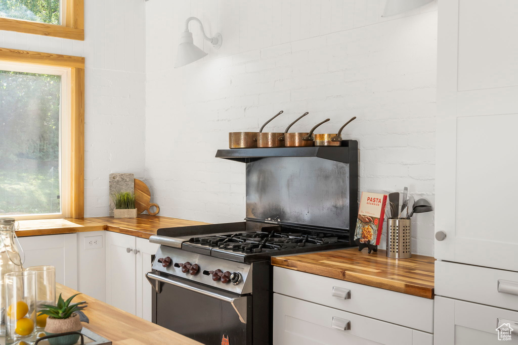Kitchen featuring butcher block counters, high end stainless steel range, and white cabinetry