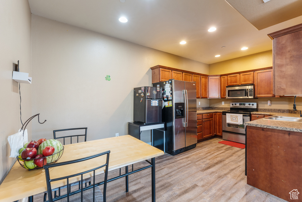 Kitchen with appliances with stainless steel finishes, light wood finished floors, brown cabinets, recessed lighting, and light countertops