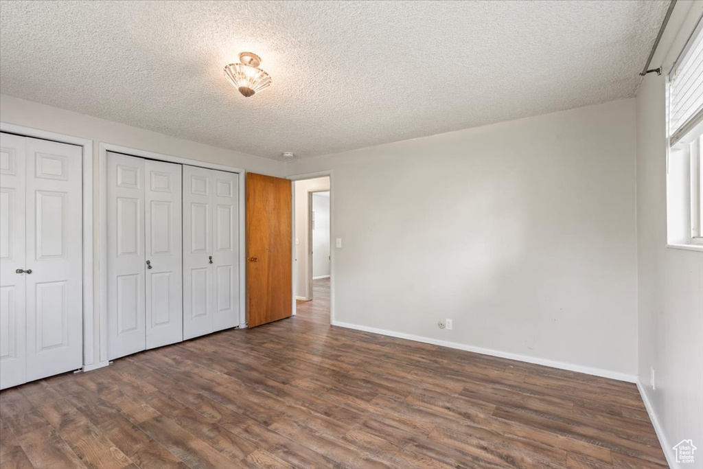 Unfurnished bedroom featuring two closets, dark wood-style floors, and a textured ceiling