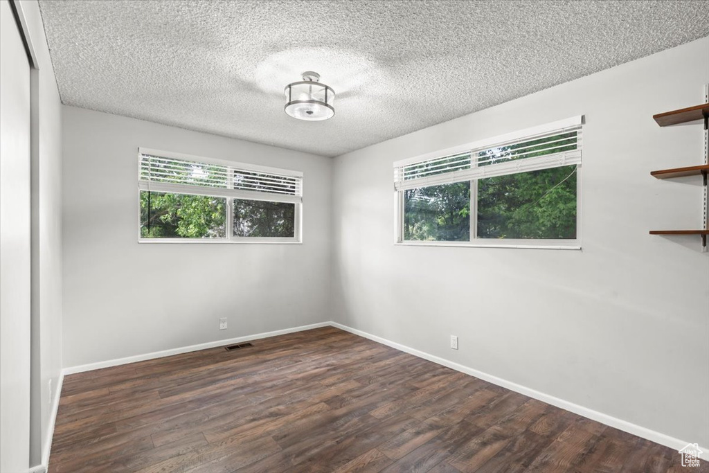 Empty room with healthy amount of natural light, wood finished floors, and a textured ceiling