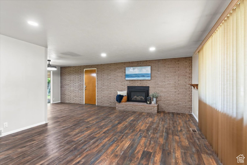 Unfurnished living room with brick wall, a fireplace, wood finished floors, and recessed lighting