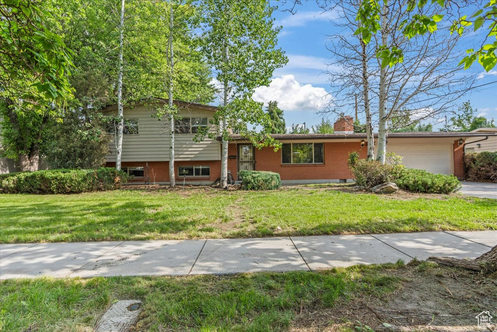 Split level home with brick siding, an attached garage, a front lawn, and a chimney