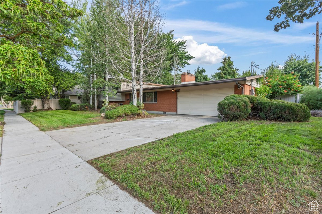 View of front facade with concrete driveway, a garage, a front yard, brick siding, and a chimney