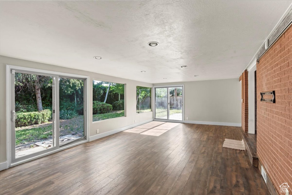 Unfurnished room featuring hardwood / wood-style flooring, brick wall, a textured ceiling, and recessed lighting