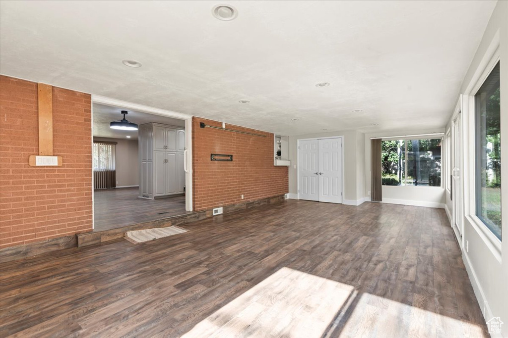 Unfurnished living room with dark wood finished floors, brick wall, and recessed lighting