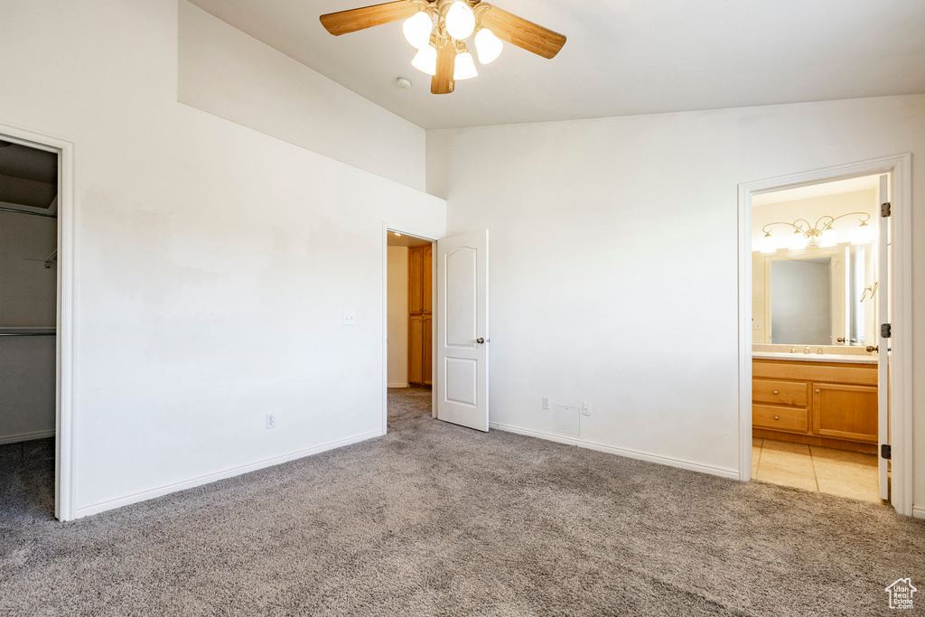Unfurnished bedroom featuring light colored carpet, vaulted ceiling, a spacious closet, connected bathroom, and ceiling fan
