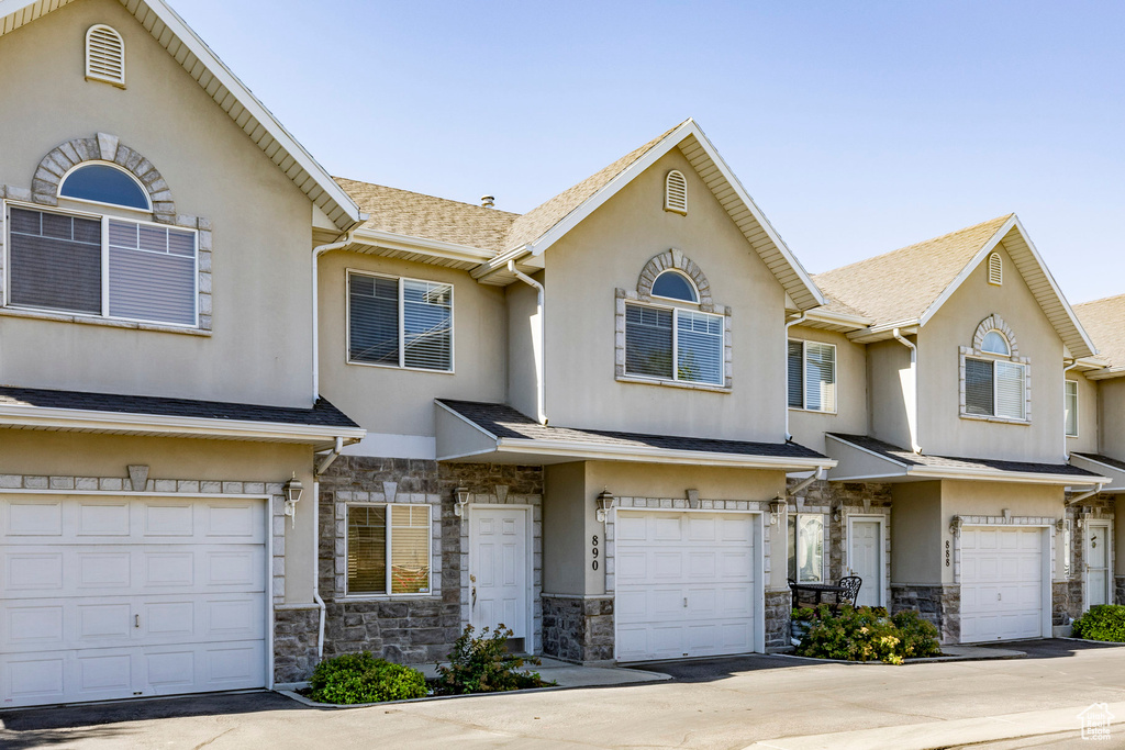 View of front of house with a garage, driveway, stone siding, and stucco siding