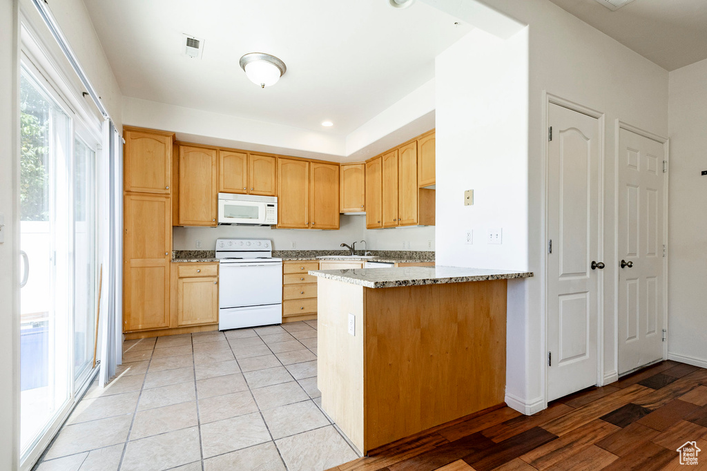 Kitchen featuring white appliances, light brown cabinets, a peninsula, and light stone counters