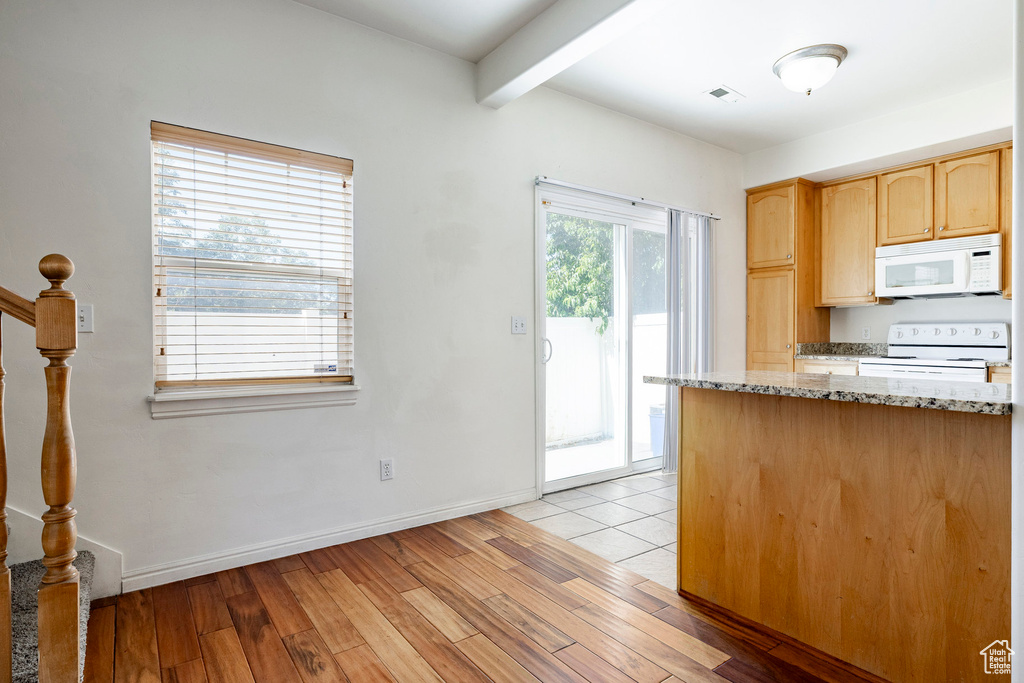 Kitchen with beamed ceiling, light brown cabinets, white appliances, light stone counters, and light wood-type flooring