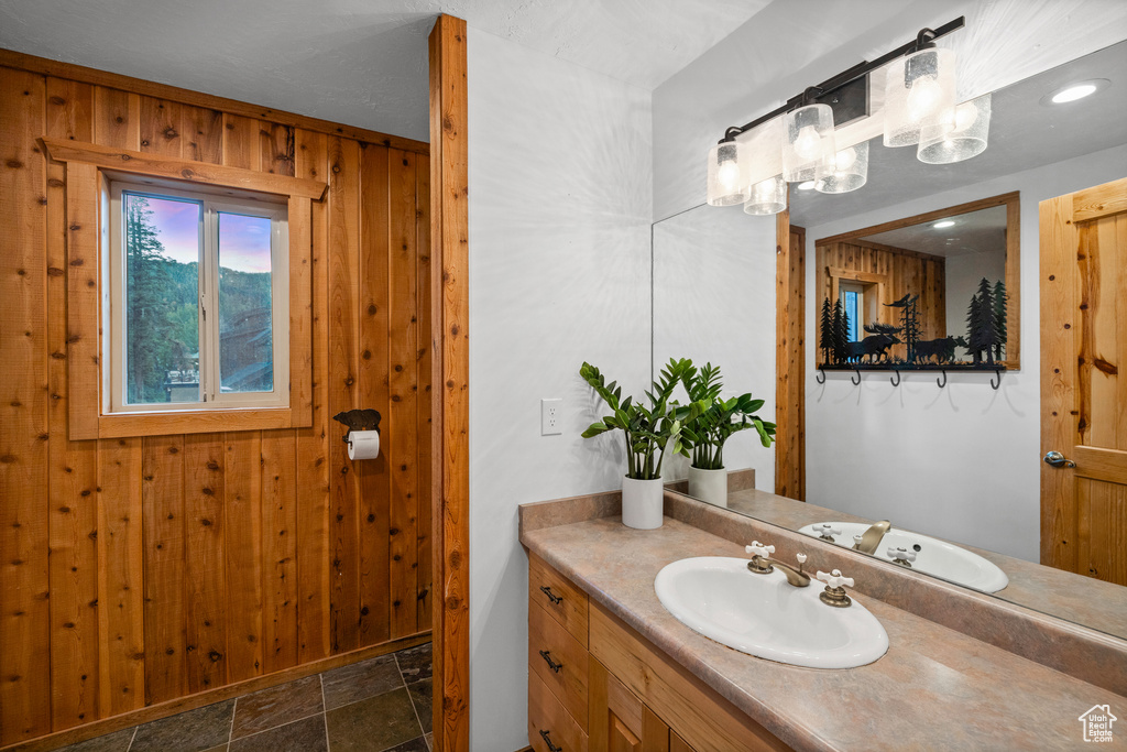 Bathroom with stone finish flooring, vanity, wood walls, and a chandelier