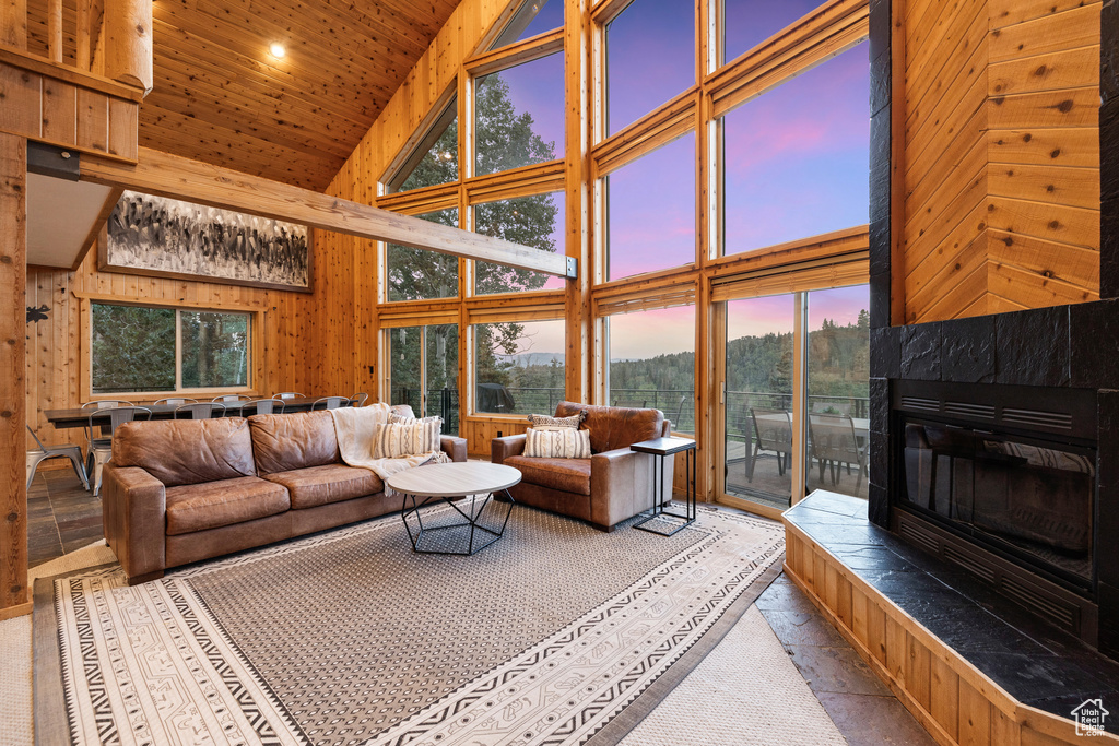 Living area featuring high vaulted ceiling, plenty of natural light, wood ceiling, a tile fireplace, and wooden walls