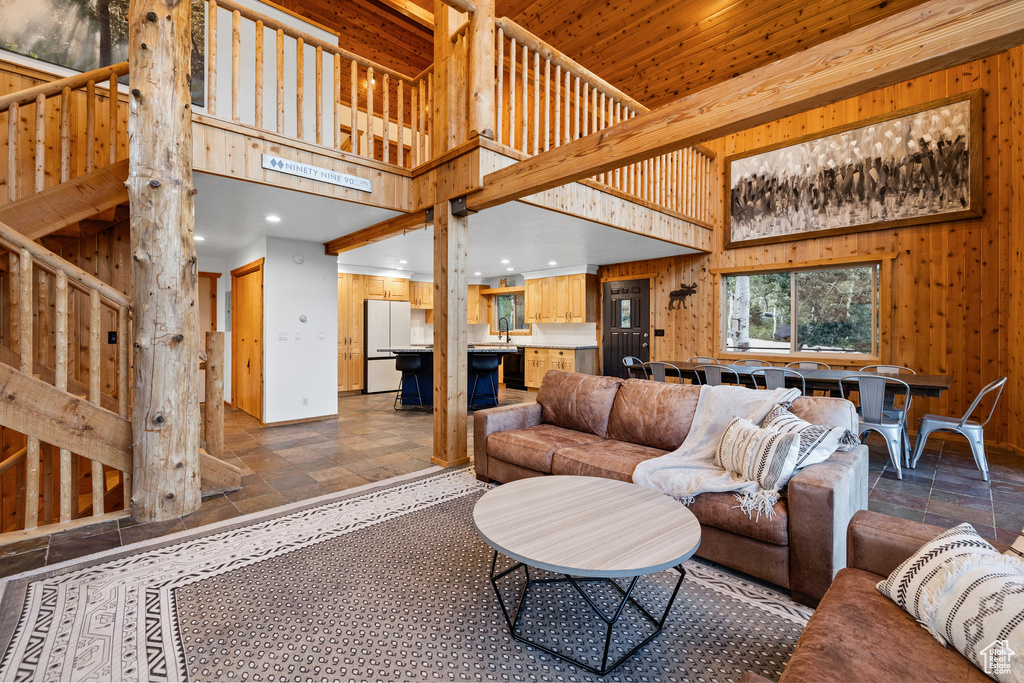 Living room with stone tile flooring, wood walls, a high ceiling, stairs, and recessed lighting