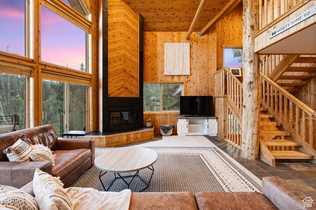 Living area featuring wooden walls, a high ceiling, wooden ceiling, a large fireplace, and stone finish floors