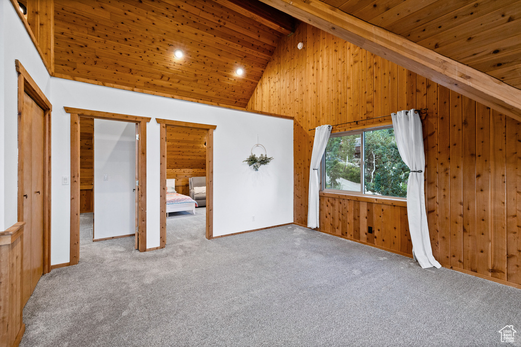 Unfurnished bedroom with high vaulted ceiling, wooden walls, carpet floors, and a wooden ceiling with exposed beams