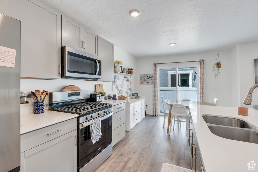 Kitchen with appliances with stainless steel finishes, light countertops, a textured ceiling, light wood-style flooring, and recessed lighting