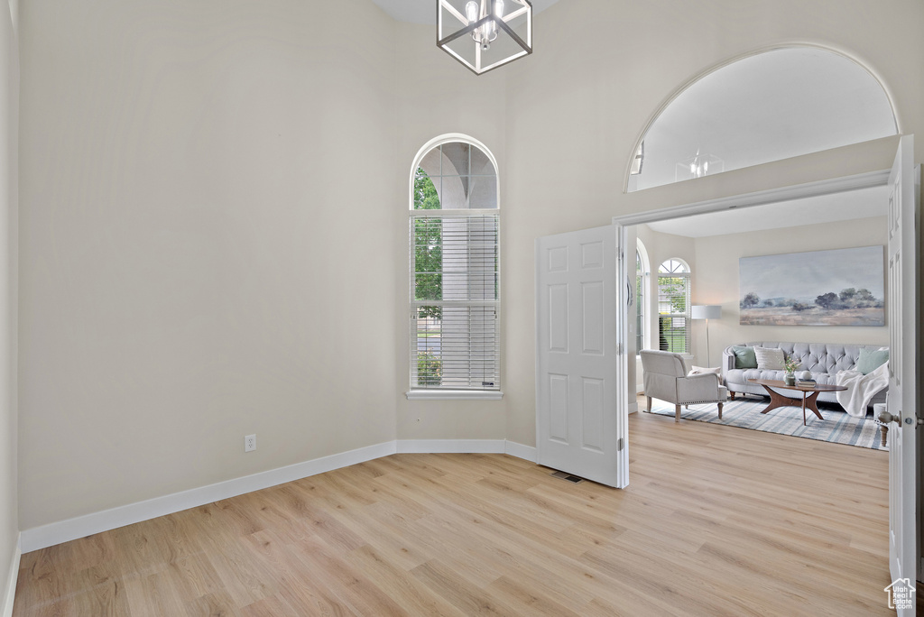 Spare room featuring light wood-style flooring, healthy amount of natural light, a chandelier, and a high ceiling