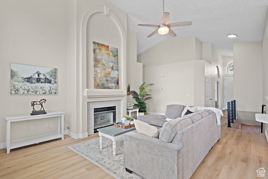 Living area with a tile fireplace, a ceiling fan, high vaulted ceiling, and wood finished floors