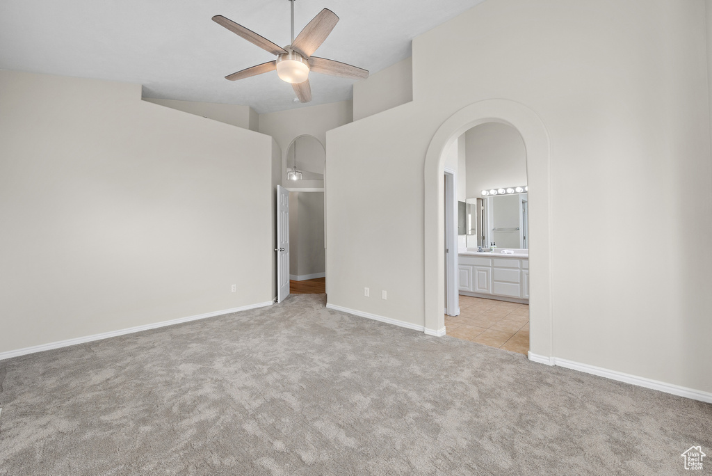 Unfurnished bedroom with arched walkways, carpet flooring, connected bathroom, and a ceiling fan