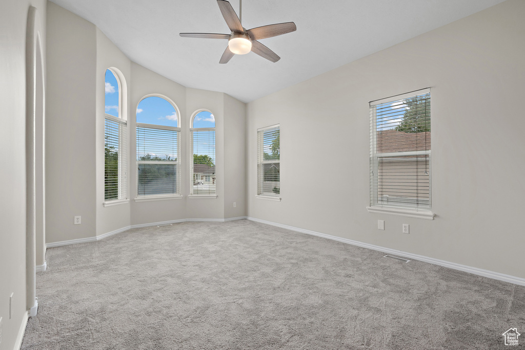 Empty room with carpet, a ceiling fan, healthy amount of natural light, and lofted ceiling