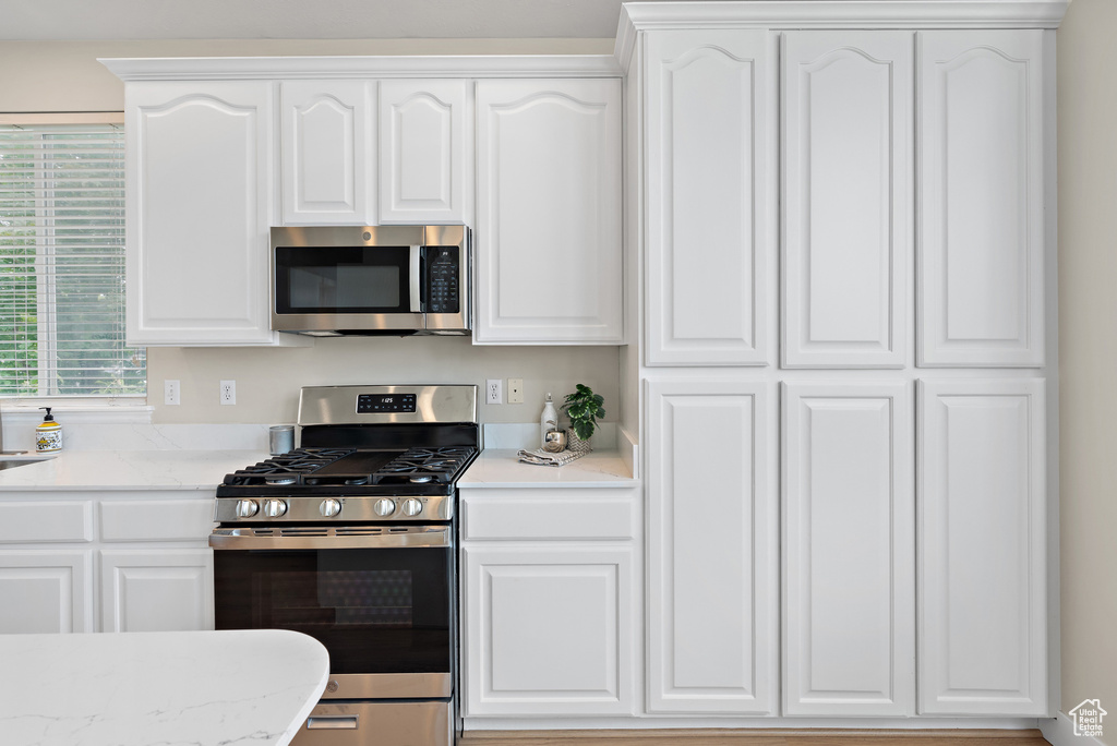 Kitchen featuring appliances with stainless steel finishes, white cabinetry, and light stone counters