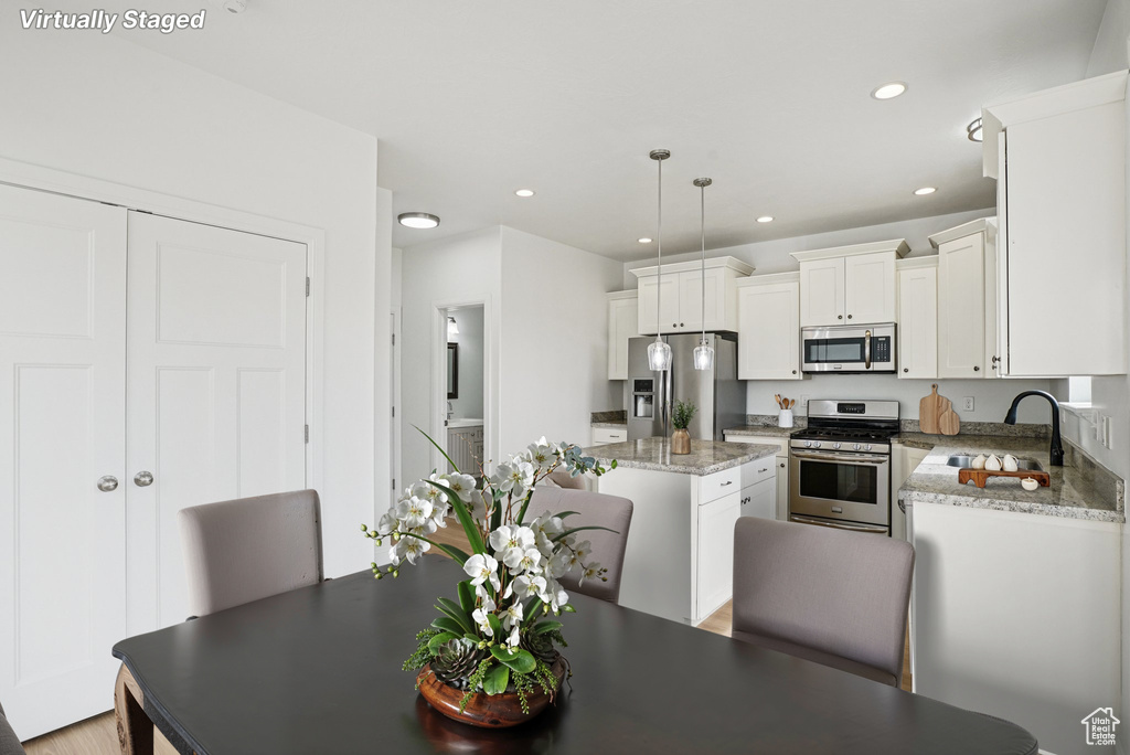 Kitchen featuring appliances with stainless steel finishes, a kitchen island, white cabinets, recessed lighting, and decorative light fixtures