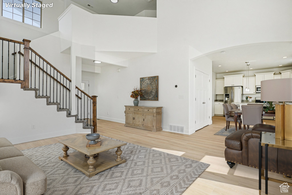 Living area featuring a towering ceiling, light wood-style flooring, arched walkways, stairs, and recessed lighting