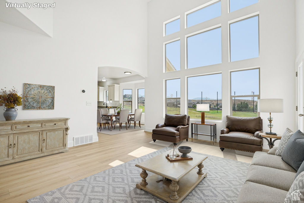 Living room featuring arched walkways, light wood-style flooring, and a high ceiling
