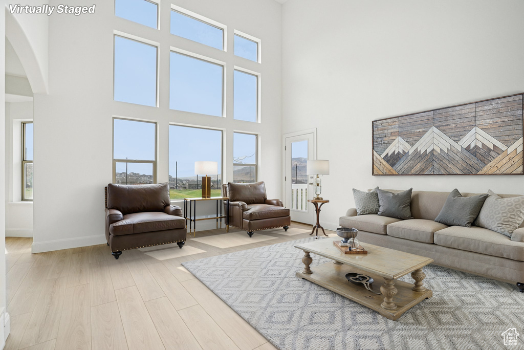 Living room with arched walkways, plenty of natural light, light wood-style floors, and a towering ceiling