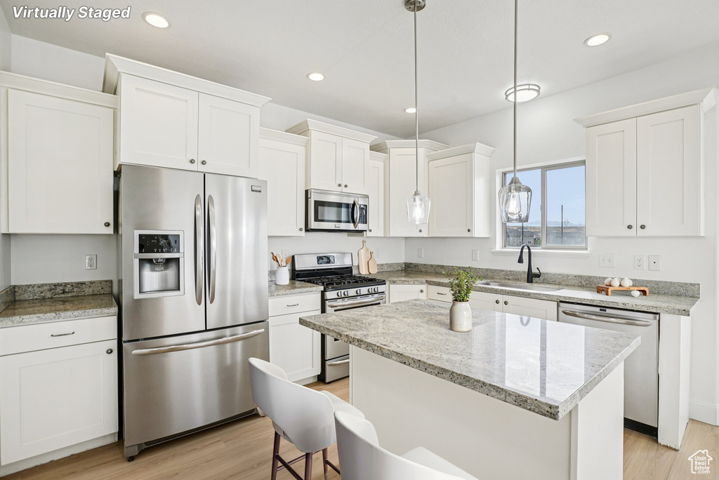 Kitchen with appliances with stainless steel finishes, white cabinetry, light wood-type flooring, recessed lighting, and pendant lighting