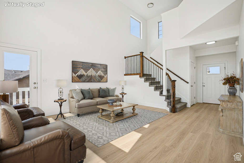 Living area with stairway, light wood-type flooring, healthy amount of natural light, and a high ceiling